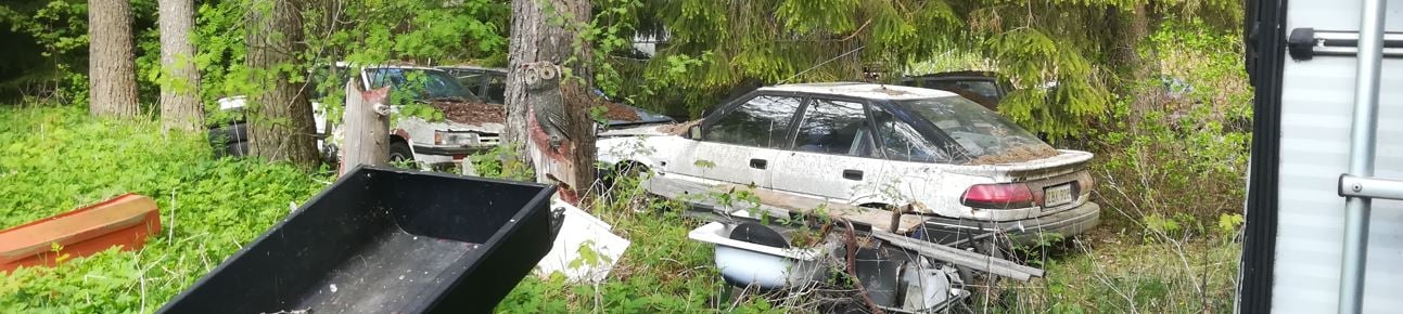 Romuajoneuvoja ja muuta romua metsän reunassa omakotitalon piha-alueella